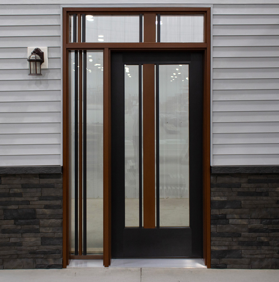 Black door large glass inserts and wood toned stiles, sidelight, and transom windows to match set in house with gray siding and brick lower half.